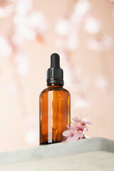 Obraz na płótnie Canvas Amber glass dropper bottle and spring cherry blossom flower on marble shelf. Skincare products , natural cosmetic. Beauty concept for face and body care, ow angle view,