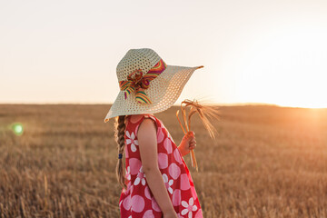 Child girl in straw hat dress in wheat field. Smiling kid in sunglasses sunset countryside. Cottagecore style aesthetic.