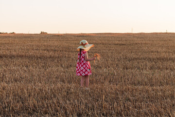 Child girl in straw hat dress in wheat field. Smiling kid in sunglasses sunset countryside. Cottagecore style aesthetic.