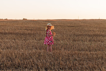 Naklejka na ściany i meble Child girl in straw hat dress in wheat field. Smiling kid in sunglasses sunset countryside. Cottagecore style aesthetic.