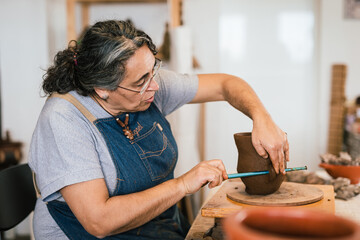 Craftswoman artisan shaping piece of clay ceramic pot with tool