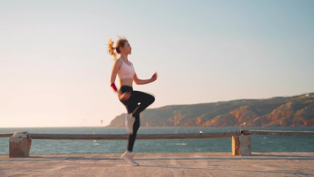 Athletic woman training jump exercise workout. Sporty caucasian female jumping cardio training with ocean and mountain landscape background. Healthy lifestyle. Sportive person outdoor