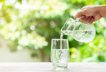 Woman hand pouring water in a glass on out of focus background.