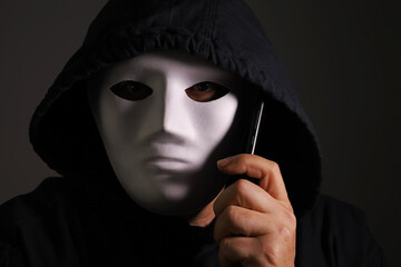 a masked man talking by smartphone on a dark background
