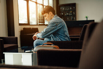 Young man traveler holding and looking mobile phone while waiting airline flight to travel at...