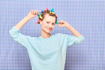 Happy woman with colorful hair curlers, and skincare product on face