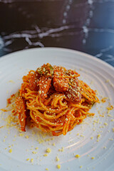 Thai fusion food style : Spaghetti with bell peppers and smoked sausage Stir-fried with spicy Thai spices and sprinkled with powdered cheese and placed in a white plate on a black marble table.