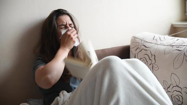 Young sick woman lying in bed reading a book cough and sneeze from common cold. Teen ill female have health issue from cold and flu with high temperature.