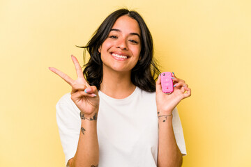 Young hispanic woman holding a keys car isolated on pink background showing number two with fingers.