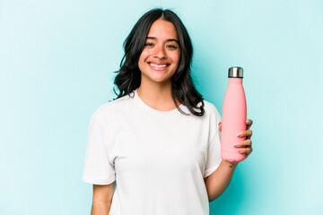 Young hispanic woman holding thermo isolated on blue background happy, smiling and cheerful.