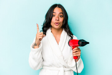 Young hispanic woman holding dryer isolated on blue background having an idea, inspiration concept.