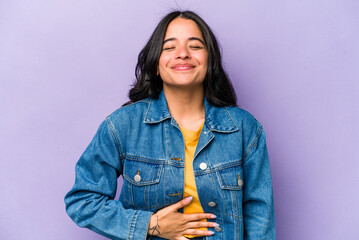 Young hispanic woman isolated on purple background touches tummy, smiles gently, eating and satisfaction concept.