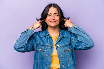 Young hispanic woman isolated on purple background covering ears with fingers, stressed and desperate by a loudly ambient.