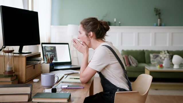 young woman come up to workplace at home with coffee cup for start remote work or distance education in the morning, sits down, turns on computer, stretches and yawns, types and focuses on screen
