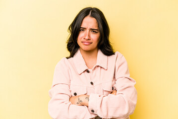 Young hispanic woman isolated on yellow background frowning face in displeasure, keeps arms folded.