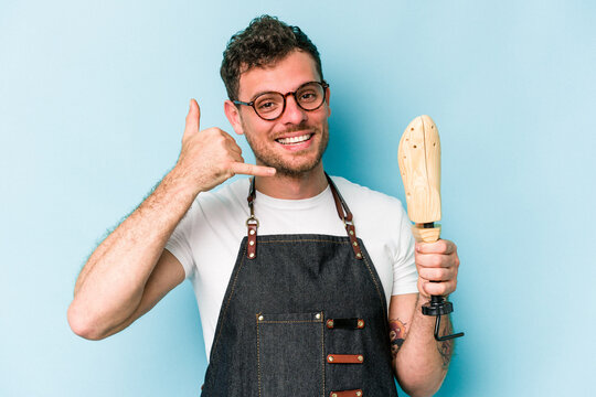 Young caucasian shoemaker man isolated on blue background showing a mobile phone call gesture with fingers.