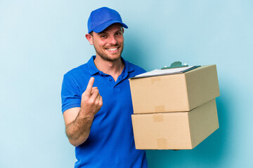 Young caucasian delivery man isolated on blue background pointing with finger at you as if inviting come closer.