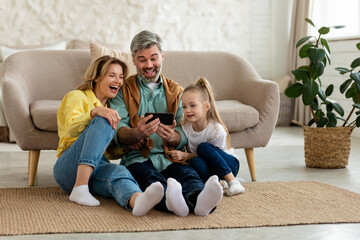 Joyful Family Using Mobile Phone Laughing Browsing Internet At Home