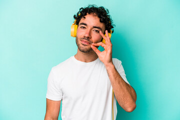 Young caucasian man listening to music isolated on blue background with fingers on lips keeping a secret.