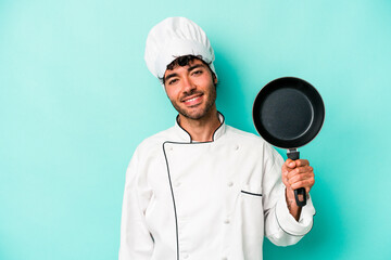 Young caucasian chef man holding flying pan isolated on blue background happy, smiling and cheerful.