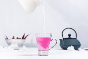 Obraz na płótnie Canvas Verter leche en una taza transparente de te rojo de bayas sobre una mesa blanca y un fondo gris claro 