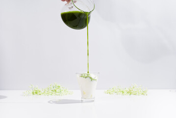 Verter té verde matcha en un vaso con helado sobre una mesa blanca y fondo gris claro	