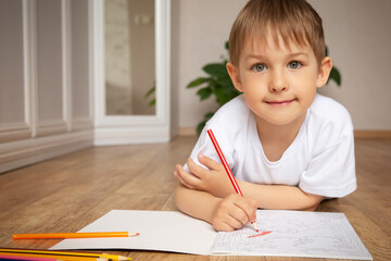 A little boy draws lying on the floor.