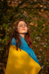 Yellow and blue fabric on the girl. Teen girl is standing a with the Ukrainian flag.