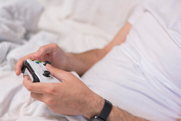 Fototapeta premium Young man playing video games at home. Close-up of a man's hands playing games console on a white controller in a white bed. Concept: free time hobby rest at home 