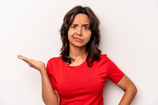 Young hispanic woman isolated on white background doubting and shrugging shoulders in questioning gesture.