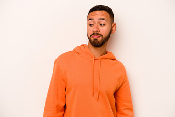 Young hispanic man isolated on white background shrugs shoulders and open eyes confused.