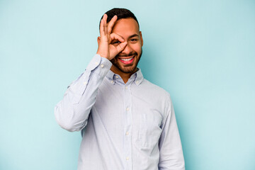 Young hispanic man isolated on blue background excited keeping ok gesture on eye.