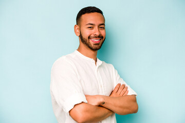 Young hispanic man isolated on blue background who feels confident, crossing arms with determination.
