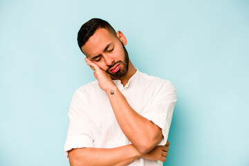 Young hispanic man isolated on blue background tired of a repetitive task.