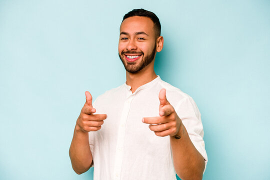 Young hispanic man isolated on blue background cheerful smiles pointing to front.