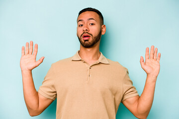 Young hispanic man isolated on blue background being shocked due to an imminent danger