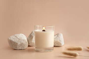 Vanilla burning candle on beige background. Warm aesthetic composition with stones and dry flowers. Home comfort, spa, relax and wellness concept. Interior decoration - obrazy, fototapety, plakaty
