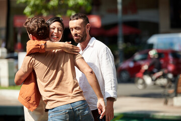 Obraz na płótnie Canvas Happy woman hugging her friend or coworker she met in park when walking with boyfriend