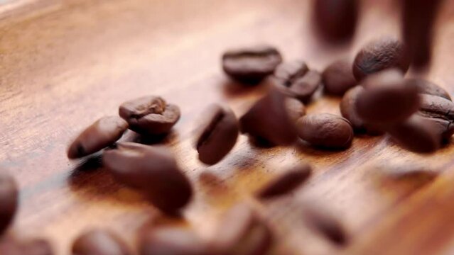 Roasted coffee beans falling on a wooden rustic bowl surface. Fragrant dark seeds . Macro. Slow motion