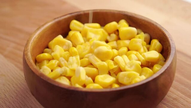 Full wooden rustic bowl with canned kernel sweet corn close-up. Sprinkling in slow motion. Close-up