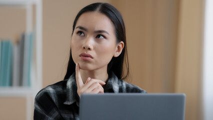 Thinking student girl asian pensive woman portrait works laptop doing online task looking for problem solution feels doubtful deep in thoughts makes decision thinks about answer difficult task