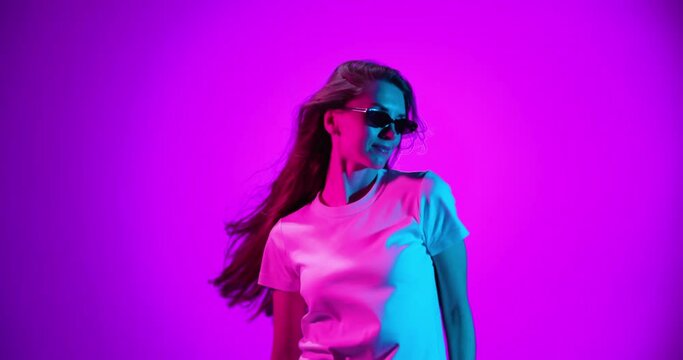 Charming young girl dancing, her hair blowing in the wind isolated on very peri color background in neon light, filter. 4K. Emotions, ad, facial expressions, youth concept