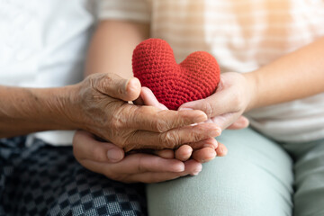 Young and senior woman holding each other hands and red yarn heart shape togetherness concept....