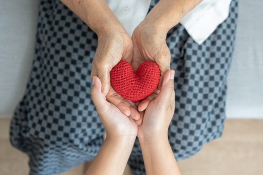 Young and senior woman holding each other hands and red yarn heart shape togetherness concept. Elderly care and protection with love from grandchild.