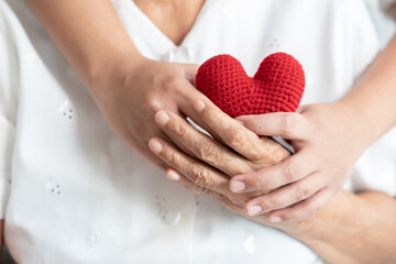 Young and senior woman holding each other hands and red yarn heart shape togetherness concept. Elderly care and protection with love from grandchild.