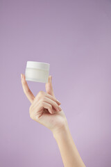Front view of hand model holding cosmetic jar in purple background for cosmetic advertising