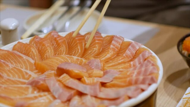 4k video of using chopctick pick slamon up from plate full of salmon sashimi, raw fish Japanese style food.