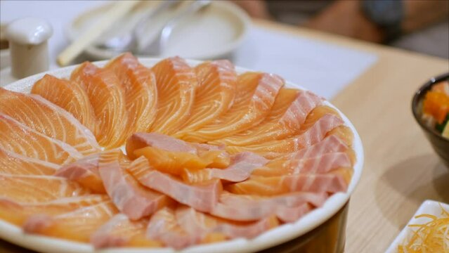 4k video of using chopctick pick slamon up from plate full of salmon sashimi, raw fish Japanese style food.