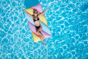 Top view of a beautiful woman in a black bikini on a colorful float in a swimming pool