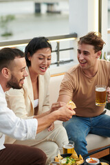 Joyful group of friends having tortilla chips with hot sauce and beer in bar